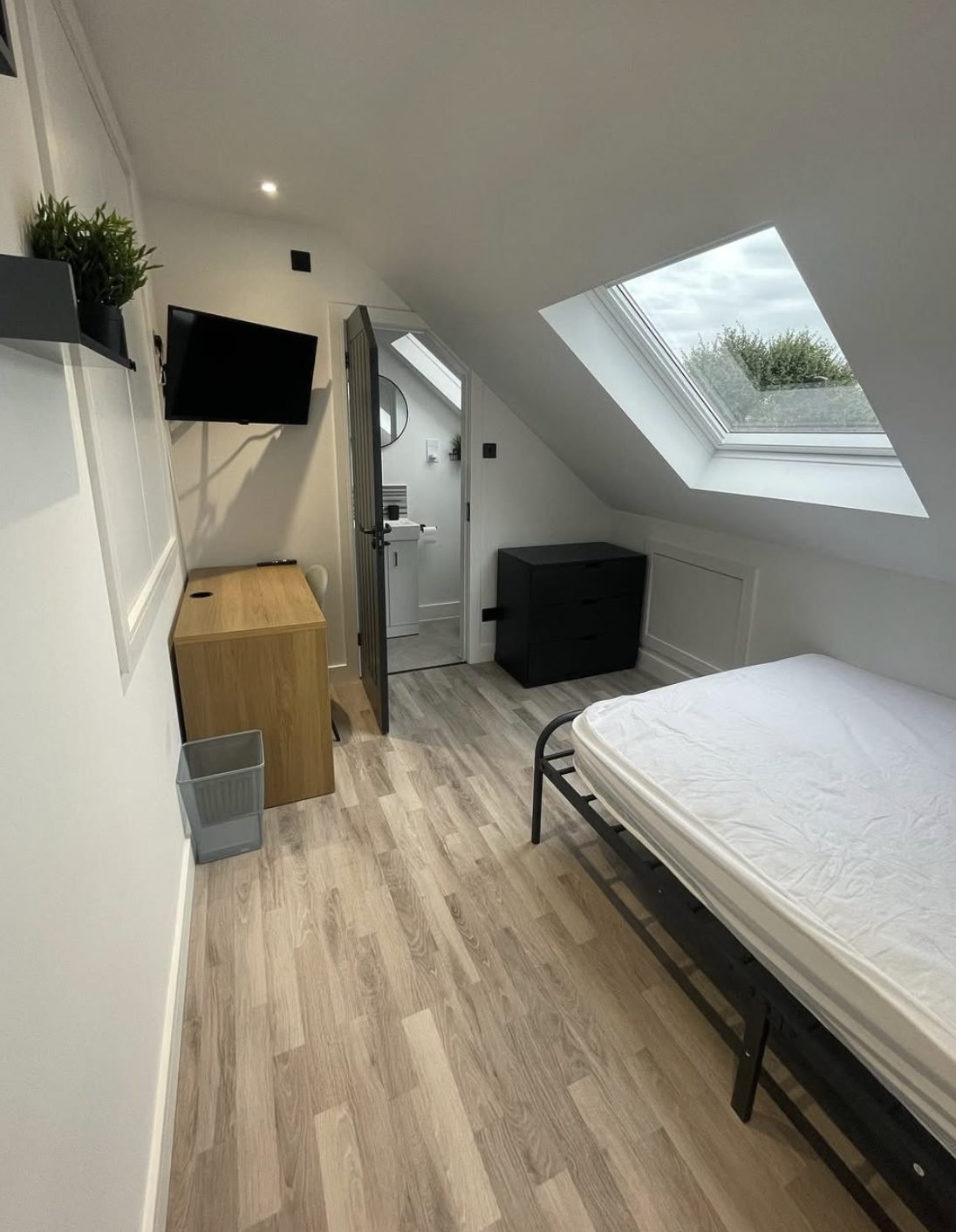 Finished loft bedroom with rooflight, wood-effect flooring, panelled walls and a door through to a loft ensuite