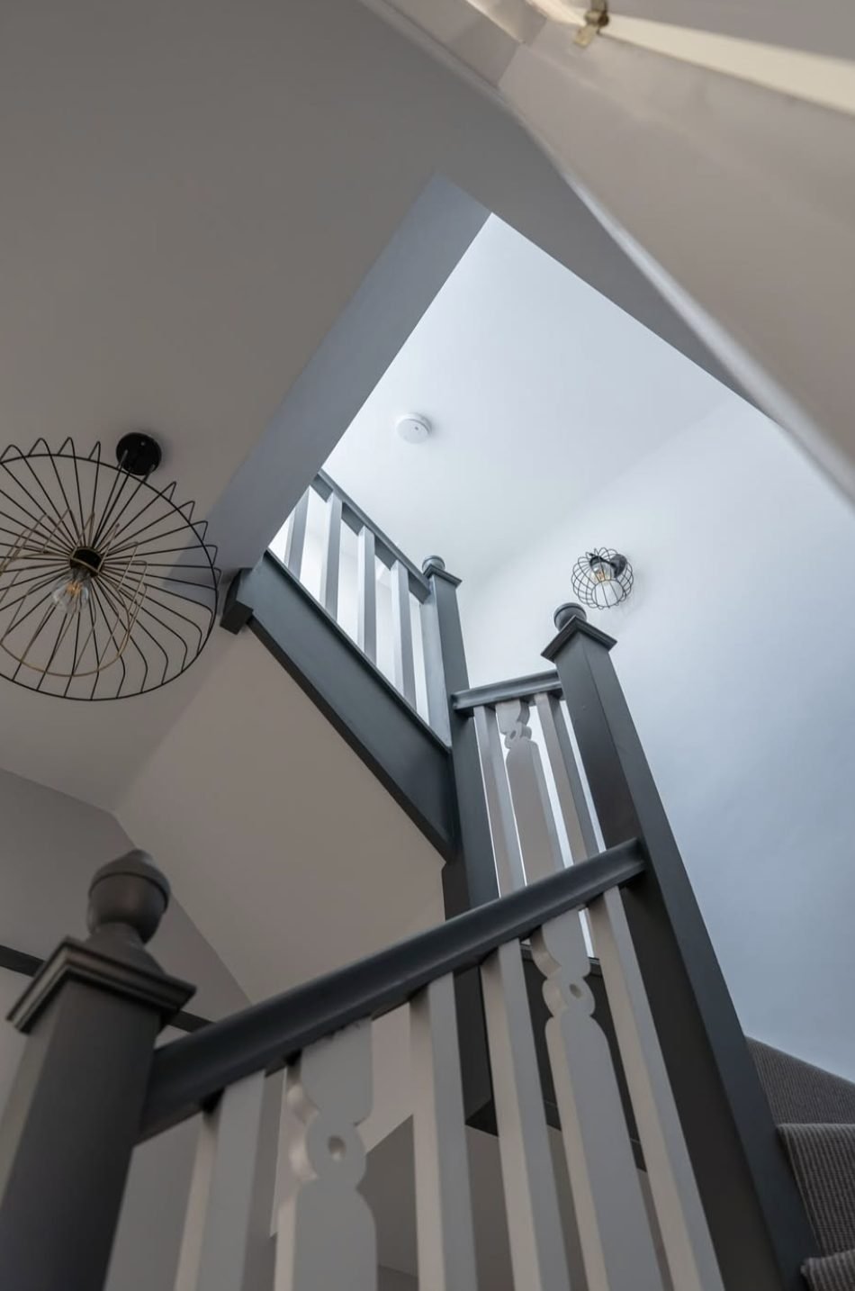 Looking up a loft staircase with grey painted handrail and newels, white spindles and wire pendant light