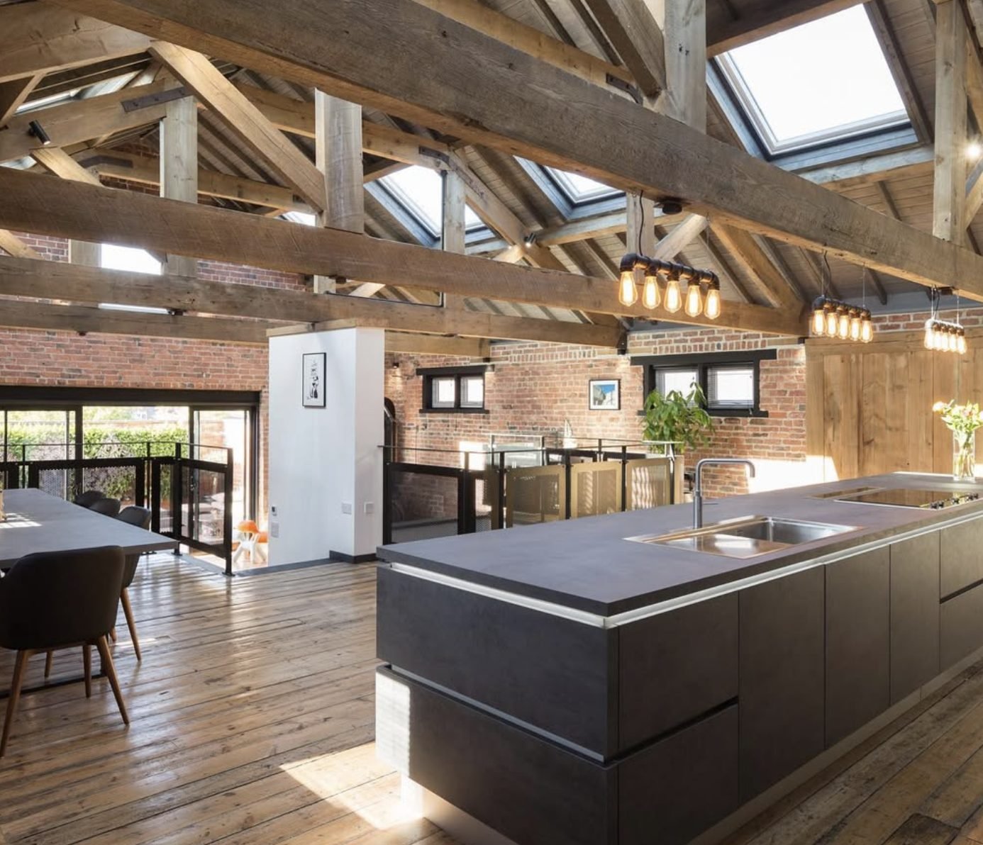 Open-plan room with exposed timber roof trusses, rooflights and a dark kitchen island